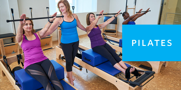 Small group Pilates class with three women on reformers taught by Pilates instructor